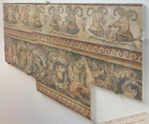 Border fragment of floor mosaic depicting rams’ heads over open wings