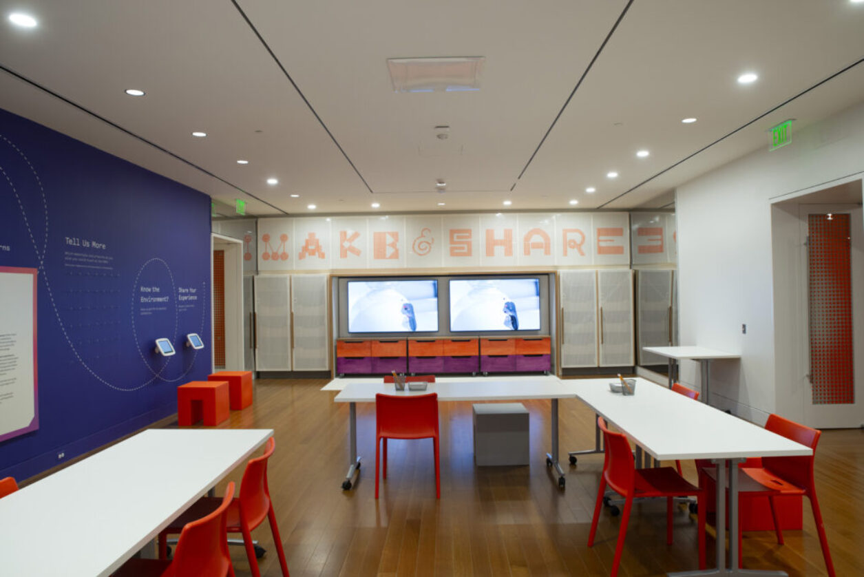 The BMA studio features red chairs and white tables with video sreens for learning.
