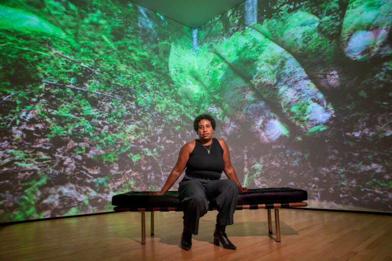 Artist V Walton sits inside of their gallery display Turn Again to the Earth in the Community Gallery at the Baltimore Museum of Art