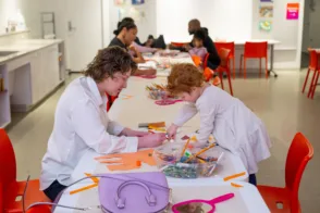 A parent and small child lean over a table and work together on a craft using colorful paper in the Joseph Education Center