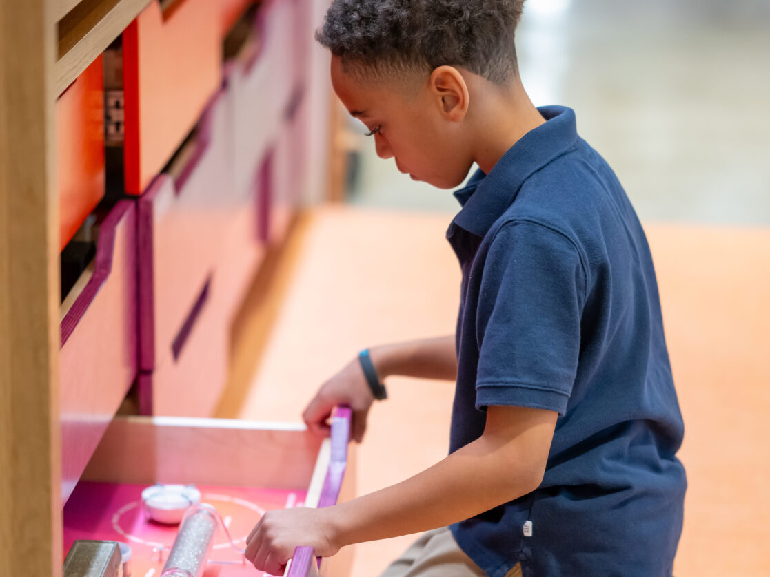 A boy with a blue shirt explores a red drawer inside the Wall of Wonder at the Baltimore Museum of Art